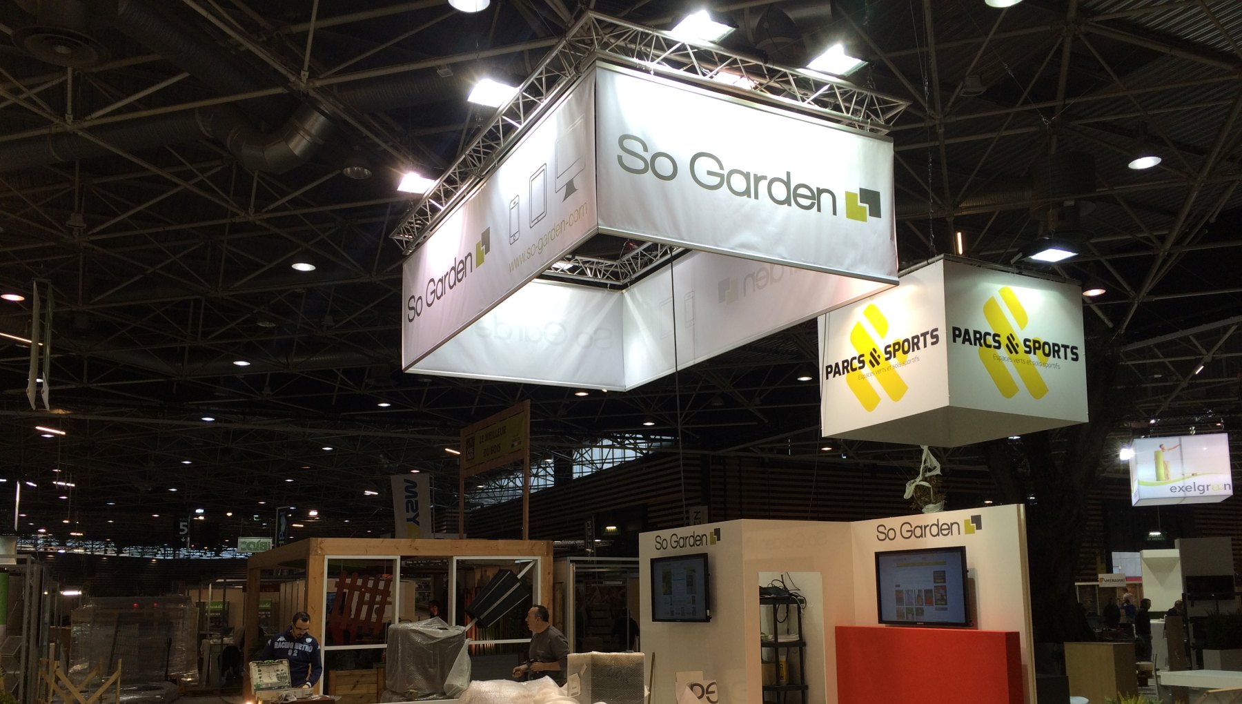Structures aluminium suspendues avec bâches imprimées et projecteurs LED au-dessus de stands sur un salon professionnel